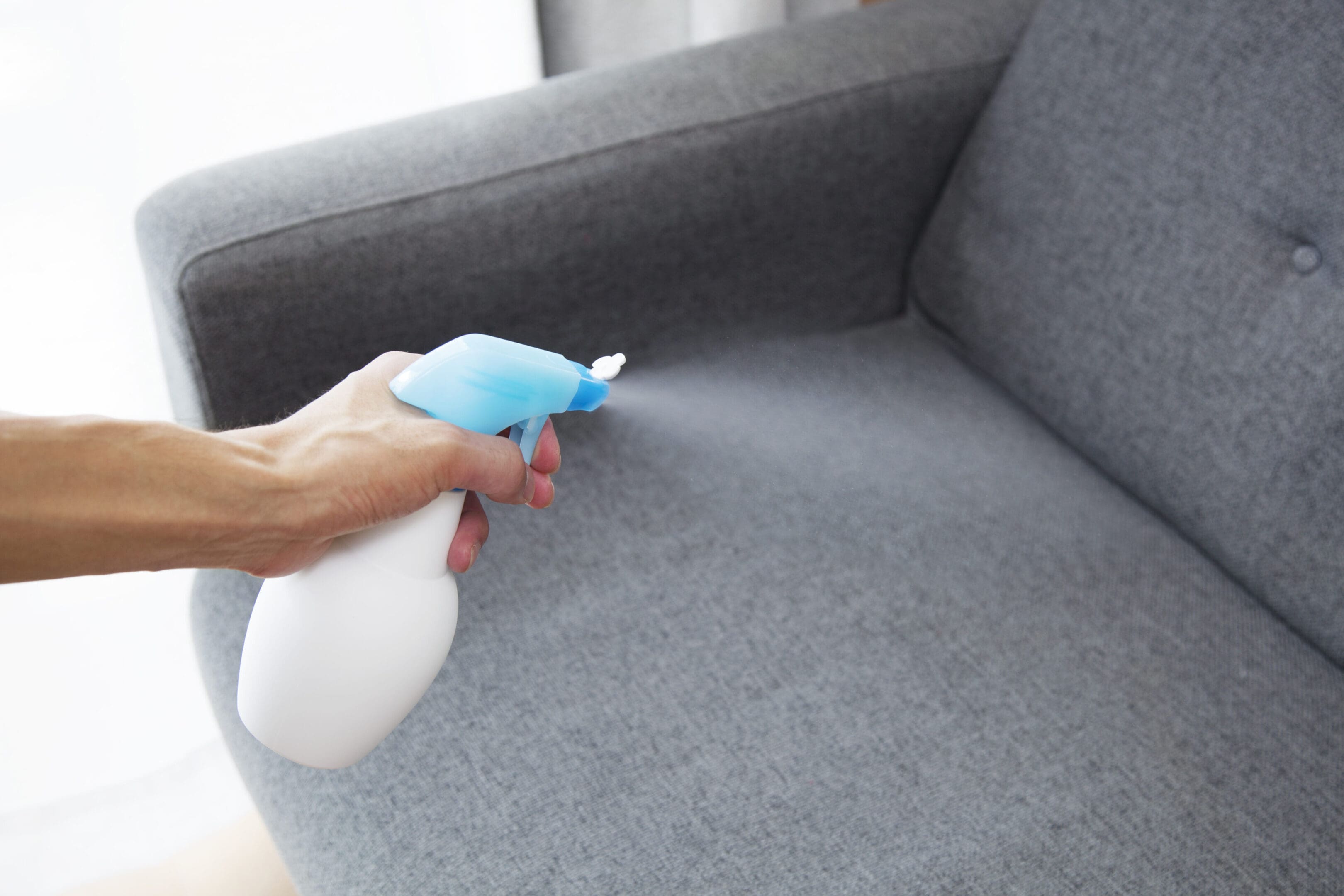 A person cleaning the arm of a couch with a spray bottle.